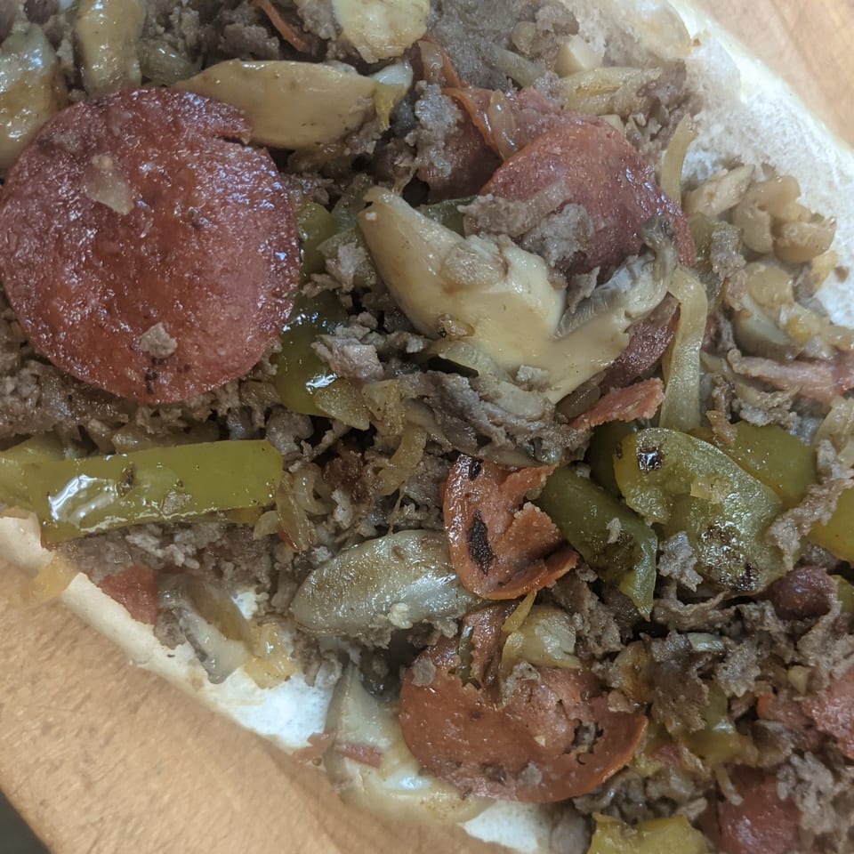 Close-up of a loaded Philly cheesesteak with steak, pepperoni, mushrooms, onions, and peppers.