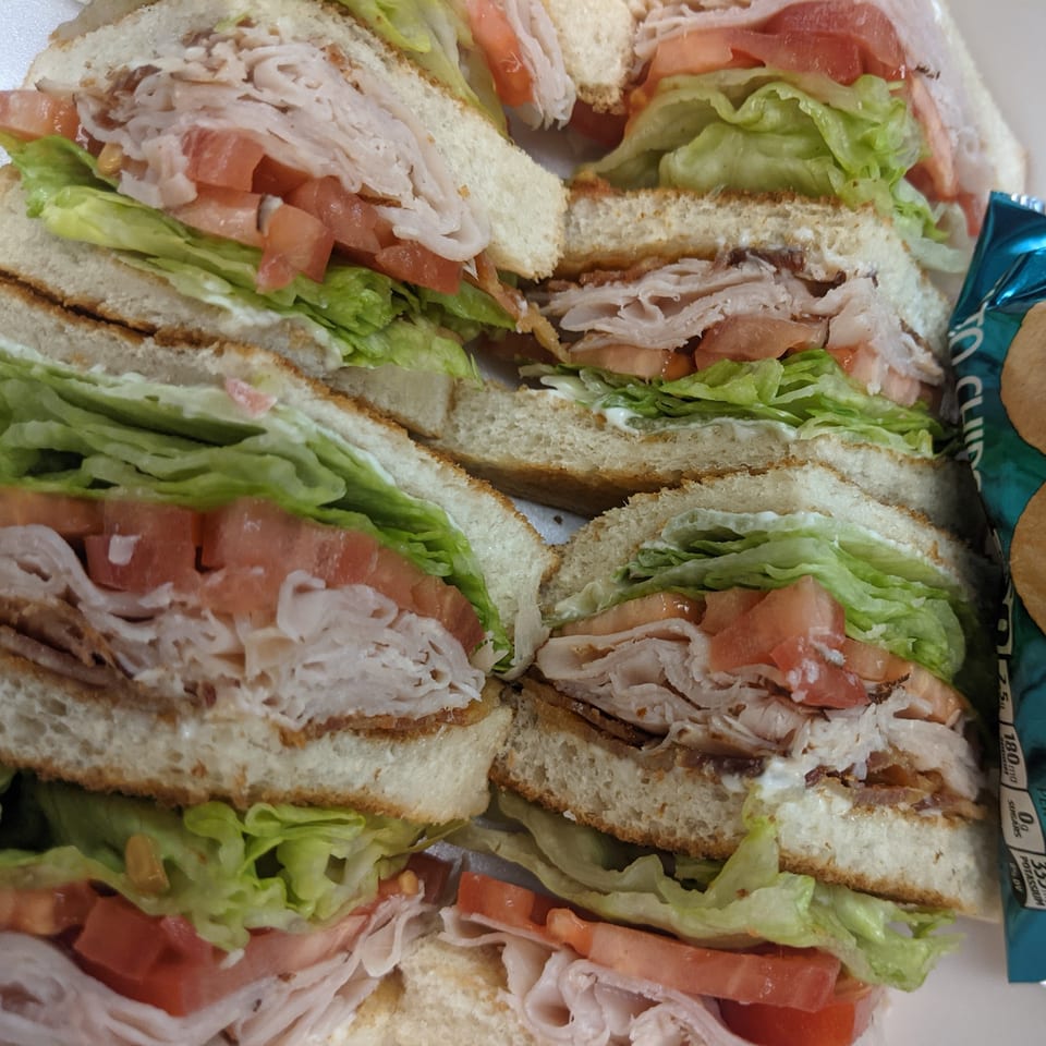 Four deli sandwiches, cut in half, with turkey, bacon, lettuce, tomato, and mayonnaise.